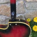 Záběr na zadní část trupu a krku elektrické kytary s červeno-černým přechodem (sunburst). Kytara má žluté lemování kolem korpusu a černý krk. Na povr…