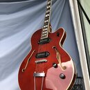 Polodupatá elektrická kytara v červeném lesklém provedení s krémovým lemováním. Nástroj má dva humbuckery, tři ovládací knofíky a stínivý mechanismus…