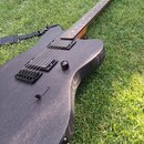 Černá elektrická kytara s matným povrchem a viditnou strukturou dřeva, položená na trávě. Nástroj má dva humbuckery, jeden ovládací knoflík a černý m…