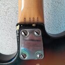 Detail zadní strany krku a spoje s tělem elektrické kytary. Na dřevěném krku je vyryjeno číslo 0 12 1. Kovová spojovací deska je přišroubovaná čtyřmi…