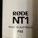 Detailní záběr na bílé tělo mikrofonu. Na povrchu je černý nápis RØDE, NT1 a text MADE IN AUSTRALIA P48. Povrch je hladký a v dobrém stavu.