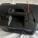 Černý plastový kryt reproduktoru s integrovanou rukojetí. Z horní části vyčnívají dva odhalené elektrické vodiče, jeden červený a jeden černý, zakonč…