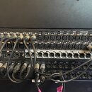 Fotografie zachycuje zadní panel rackového audio zařízení s velkým množstvím zapojených XLR konektorů. Na horní hraně panelu jsou nápisy: "our raft",…