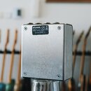 Záběr na zadní stranu efektového pedálu z broušeného kovu stříbrné barvy. Na horní části je nalepený štítkem s nápisy „strymon“, „CE“, symbol recykla…