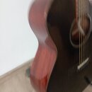 Detailní pohled na tmavě hnědou akustickou kytaru s vyvedeným Maserováním dřeva na boky. Je vidět část korpusu, hmatník s řidami strun a otvor rezona…