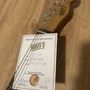 Fotografie zachycuje hlavu elektrické kytary z jasného dřeva a doprovodný certifikát pravosti. Na hlavě je vidět nápis RELIC a logo Henry's. Certifik…