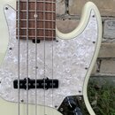 Detail elektrické basové kytary v krémové barvě s hnědým hmatníkem z dřeva. Nástroj má bílo-perleťový pickguard a dva černá snímače. V pravé dolní čá…