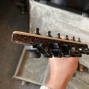 Detailní pohled na hlavu elektrické kytary s černými ladicími kolíky. Horní hrana je bílá a boční strana je opatřena černým třpytivým povrchem. Na fo…