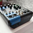 Kompaktní míchací pult v černo-šedém provedení s modrými detaily. Na přední straně je nápis MIXING CONSOLE MG06 a logo YAMAHA. Zařízení obsahuje něko…