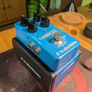 Modrý efekt pedál s nápisy FLASHBACK a tc electronic, umístěný na své originální krabici. Na horní straně jsou čtyři černé ovládací knoflíky a jeden…