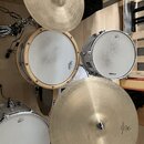 Sada bicích bubnů a činelů v bílé a dřevěné barvě. Na jednom z bubnů je vidět logo Sonor, na jiném nápis Tama. Soubor obsahuje dva činely z mosazi a…