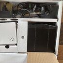 V bílé krabici se nachází černý elektronický přístroj s nápisem PRO PT 40 a k němu přibalený napájecí adaptér s černým kabelem. V horní části je vidě…