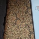 Fotografie zachycuje úzký, obdélníkový předmět, pravděpodobně pouzdro na hudební nástroj. Povrch je potažen látkou s hnědo-zlatým ornamentálním vzore…
