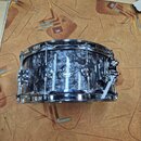 Stříbrný malý buben s černobílým mramorovaným povrchem a chromovaným kováním. Na korpusu je umístěno logo DW s nápisem "dw" a pod ním text "DRUM WORK…