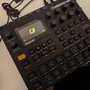 Černý sampler a sekvencer s nápisem Elektron. Zařízení obsahuje displej s logem v podobě žlutého písmene Z a nápisem Digitakt, několik otočných poten…