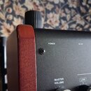 Detailní pohled na roh kytarového komba s černým předním panelem a dřevěným bočním krytem v hnědé barvě. Na panelu jsou bílé nápisy POWER, AC-IN, MAS…