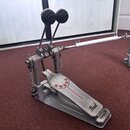 Dvojpedál na bicí v stříbrné kovové barvě. Na šlapce je vidět logo Pearl a červený dekorační pruh s pěti červenými kruhy. Povrch vykazuje mírné známk…