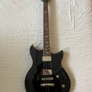 Černá elektrická kytara s tmavým hmatníkem a bílými ladícími kolíky. Na hlavě je viditelné logo Yamaha. Tělo má dva humbuckery, jednu tónovou a jednu…
