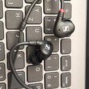 Černé šupátkové sluchátka s drátovým připojením položená na počítačové klávesnici. Na obou sluchátkách je bílé logo značky Sennheiser. Pravé sluchátk…
