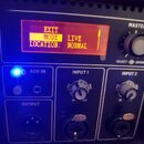 Detailní pohled na ovládací panel elektronického zařízení s červeným displejem, na kterém je text EXIT, MODE: LIVE a LOCATION: NORMAL. Panel obsahuje…