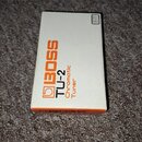 Bílá krabice od ladícího pedálu s oranžovými a černými nápisy. Na přední straně je uvedeno logo BOSS, model TU-2 a text Chromatic Tuner. V pravém hor…