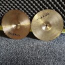 Dvě mosazné činely s viditelným rakováním povrchu. Na levém činelu je nápis istanbul Agop Made in Turkey. Pravý činely nese obrácený nápis istanbul A…