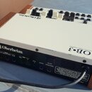 Bílá klávesová jednotka s dřevěnými bočními panely. Na horní části je nápis Oberheim a model OB-3 Drawbar Organ Expander. Přední panel obsahuje logo…