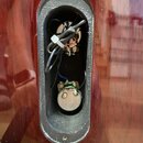 Detailní pohled do oválného výřezu v tmavě červeném lakovaném dřevě. Uvnitř jsou vidět elektrické součástky, vodiče a bílá plastová stahovací páska.…