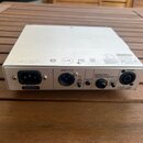 Stříbrné zařízení s kovovým šasi umístěné na dřevěném stole. Na zadním panelu jsou konektory AC INPUT, DIRECT OUT, EQ PRE-POST, AUX IN, HEADPHONES -…