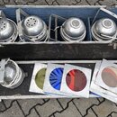Sada stříbrných kovových reflektorů umístěných v černém přepravním kufru a rozložených před ním. K dispozici je celkem deset kusů svítidel s kovovými…