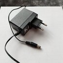 Černý síťový adaptér s plastovým tělem a evropskou vidlicí. Na boku je viditelný štítek s technickými parametry a logem YAMAHA. Adaptér má připojený…