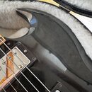 Detailní pohled na černý lakovaný korpus elektrické kytary v otevřeném pouzdře s šedým polstrováním. Na povrchu laku jsou viditelné drobné škrábance…