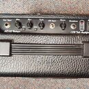 Černý kytarový kombo zesilovač v koženkovém potahu. Na ovládacím panelu jsou nápisy BEHRINGER, AC101 Vintage Amplifier a 15W Tube Amplifier. Panel ob…