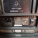 Detail zadní strany černého přístroje s logem a nápisem behringer DR115 DSP. Je zde vidět napájecí vstup, vypínač POWER a štítky s technickými inform…