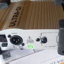 Stříbrná DI box s černými gumovými nárožníky. Na horní části je nápis ULTRA-DI a text PROFESSIONAL BATTERY / PHANTOM POWERED DI-BOX. Na zadním panelu…