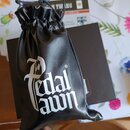 Černý stahovací vak z umělého materiálu s bílým nápisem „Pedal pawn“ a symbolem registrované znáčky ®. Vak je umístěn na černé krabici a v pozadí je…