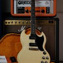 Elektrická kytara s krémovým povrchem, černým pickguardem a dvěma humbuckery, umístěná v otevřeném černém kufru s oranžovou výstuhou. Na hlavě kytary…