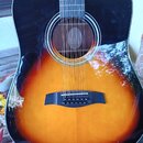 Akustická kytara s tělem v barvě sunburst (přechod od černé přes červenou k žluté). Kytara má černý lem kolem otvoru rezonátoru a černý kobylník s př…