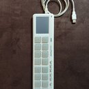 Bílá MIDI kontrolér s názvem KORG nanoPAD2. Zařízení má mřížku 16 čtvercových padů v rozložení 4x4, malý displej v horní části a řadu ovládacích tlač…