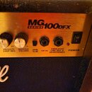 Detail ovládacího panelu kytarového komba v zlaté barvě. Na panelu je nápis MG100DFX SERIES a tři otočné knoflíky s popisky REVERB LEVEL, EFFECTS LOO…