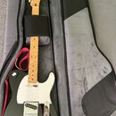 Černá elektrická kytara typu Telecaster s bílým pickguardem a světle hnědým javorovým hmatníkem v otevřeném černém pouzdře. Na hlavě kytary je vidite…