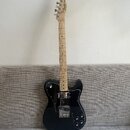 Černá elektrická kytara s černým pickguardem a světlým hnedým hmatníkem. Na hlavě je nápis Fender Mexico. Kytara má dva snímače a tři ovládací knoflí…