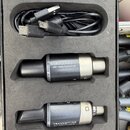 Černá krabice s pěnovým vložkem obsahuje dva cylindrické moduly a černý USB kabel. Horní modul má nápis RECEIVER MW-1 WIRELESS SYSTEM. Dolní modul ne…