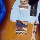 Elektrická kytara typu Telecaster v barevném přechodu od žluté po tmavě hnědou s bílým pickguardem a javorovým hmatníkem. Na bílém plastu je nálepka…