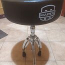 Černý bubeníckýstool s kulatým polstrovaným sedadlem z umělé kůže. Na boku sedadla je bílé logo s nápisem MAPEX™. Nástroj má chromovaný třínohý stoja…