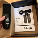Černý kondenzátorový mikrofon s nápisem AKG P120 a logem značky. Vedle něj je v krabici položen černý držák mikrofonu a uživatelský manuál s nápisy P…