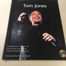 Fotografie znázorňuje černou zpěvníkni knihu s portrétem muže s mikrofonem. Na obálce je zlatým a bílým písmem nápis YOU'RE THE VOICE a Tom Jones. Do…