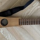 Dřevěný strunný nástroj s tělem ve tvaru trapézu a hnědým povrchem. Na hlavě je viditelné logo „Martin guitar“. K nástroji je přiložen černý popruh s…