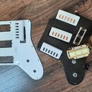 Dvě plastové vrhy (pickguardy) do elektrické kytary, jeden v bílé a druhý v černé barvě. Černý vrch obsahuje tři bílé snímače s viditelnými měděnými…