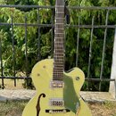 Žlutá polodupatá elektrická kytara značky Gretsch s tmavým hmatníkem a zeleným pickguardem. Na hlavě je nápis GRETSCH, na spodní části mostu je logo…